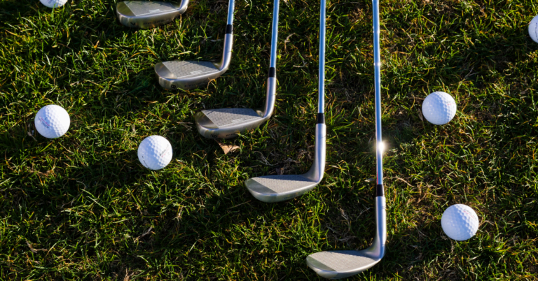 Golf irons and golf balls laying on grass.