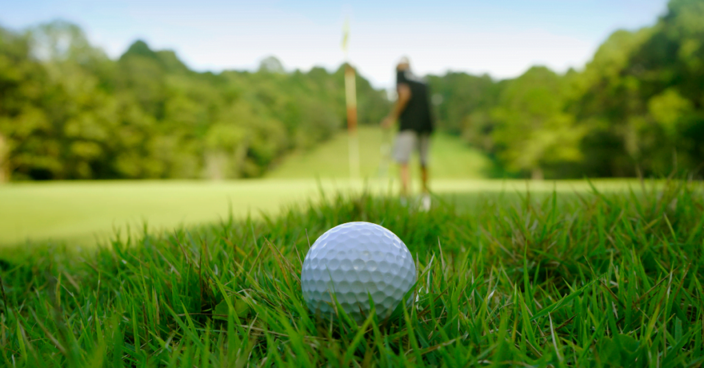 Golf ball in the grass with a golfer standing in the background.