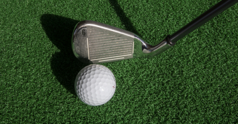 Golf ball in front of a golf club on the grass.