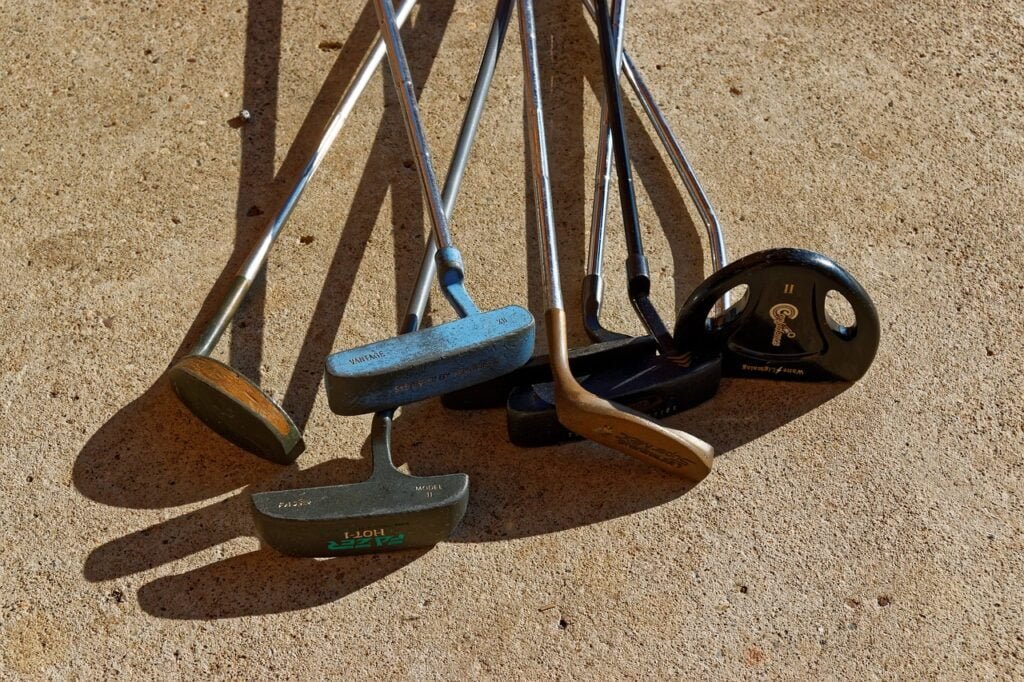 Pile of different style putters on the sand.